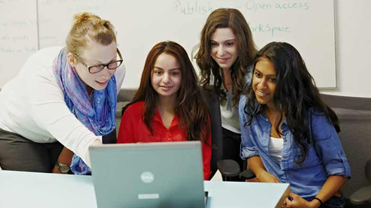 Four students gathered around a laptop, working together.