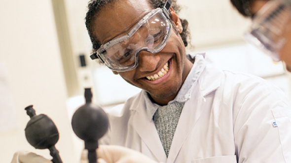 A black male student in a science lab holding two science instruments