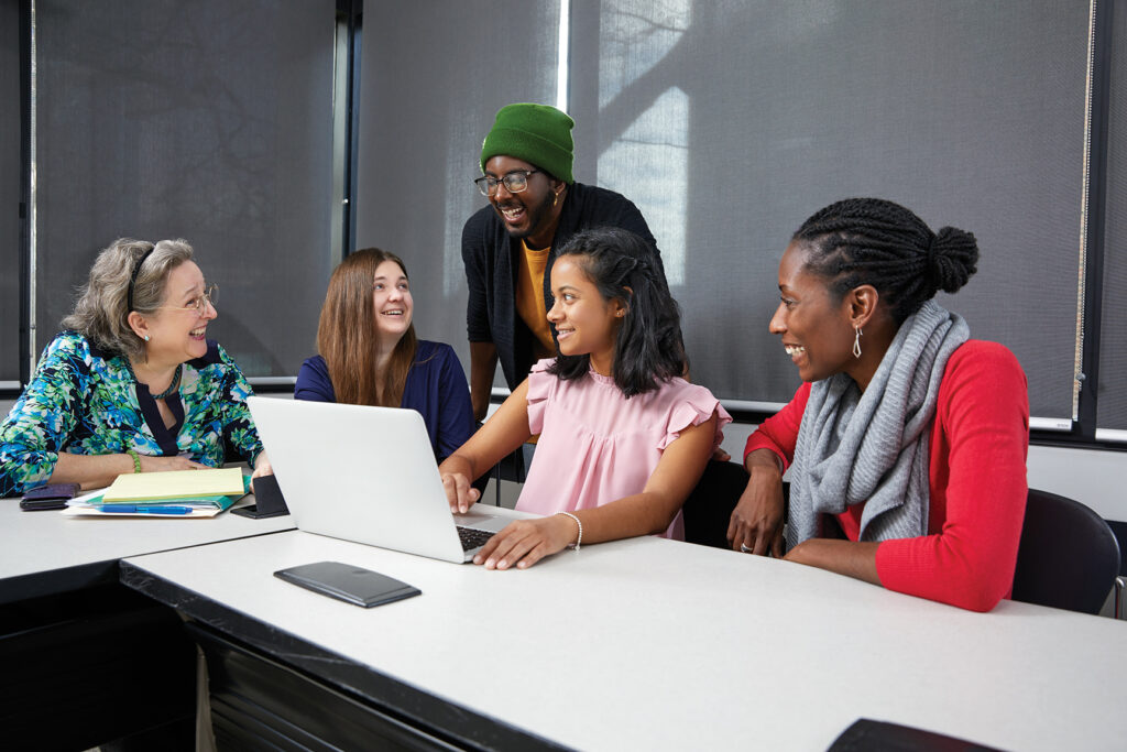 Group of students collaborating around a laptop.