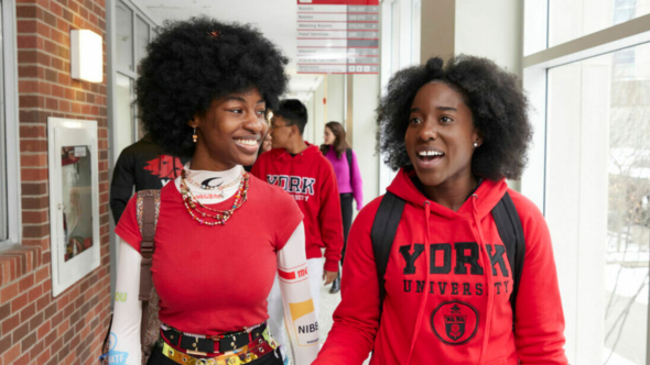 Two Black female students walk and talk while smiling at the York University campus. 
