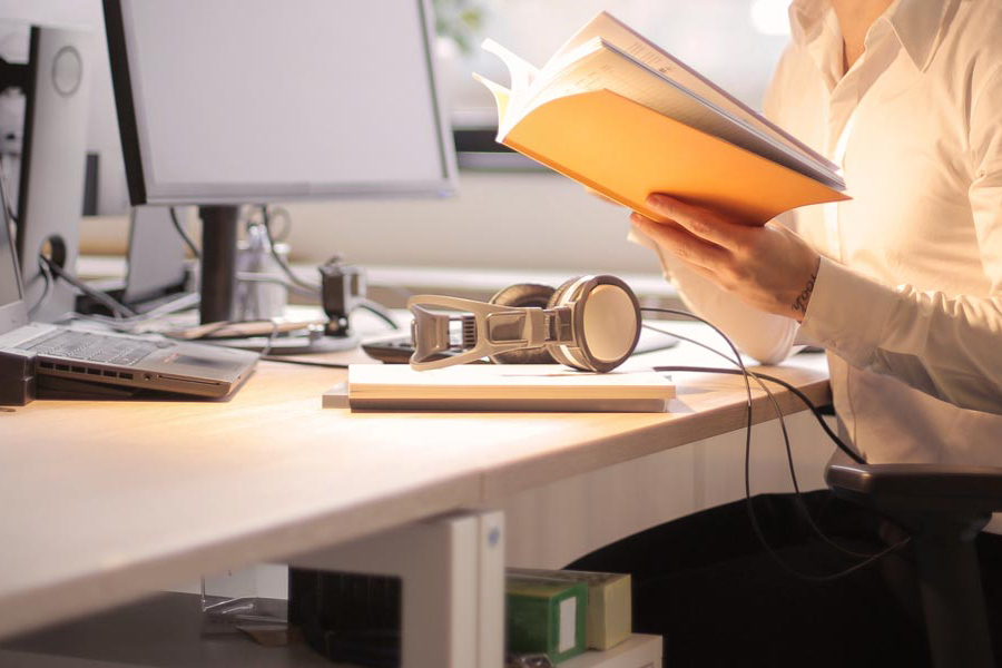 Person reading book in front of computer