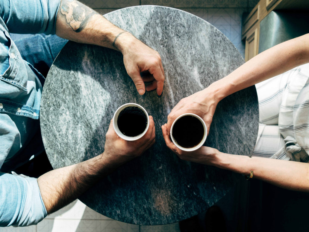 Two people talking and drinking coffee at a cafe table