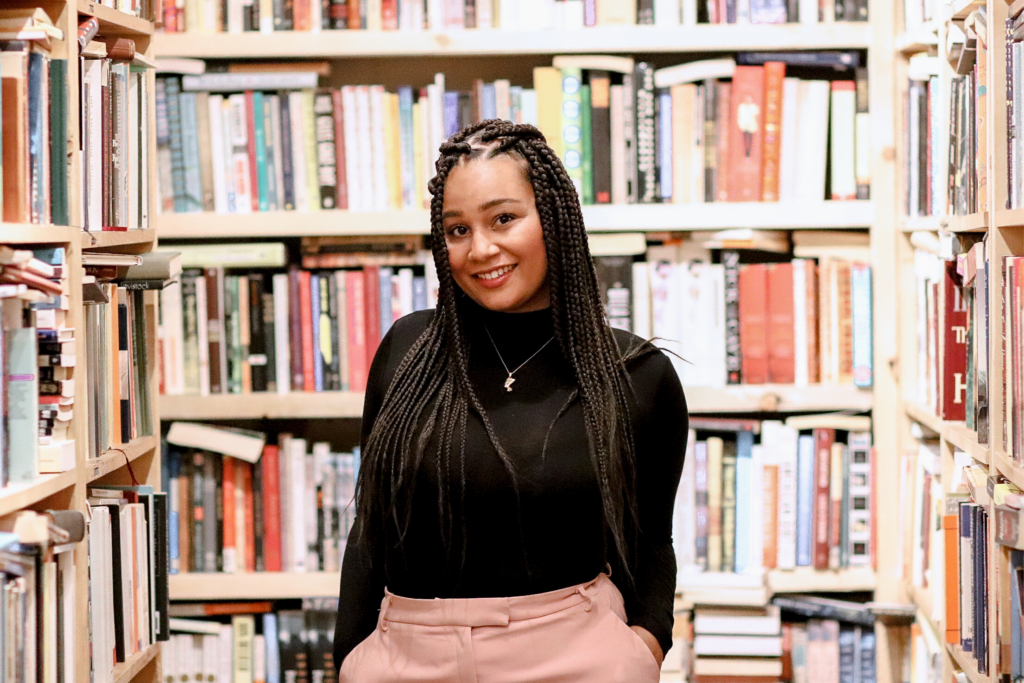 Tiyahna Ridley-Padmore stands in a a bookstore, surrounded by shelves of books, smiling at the camera.