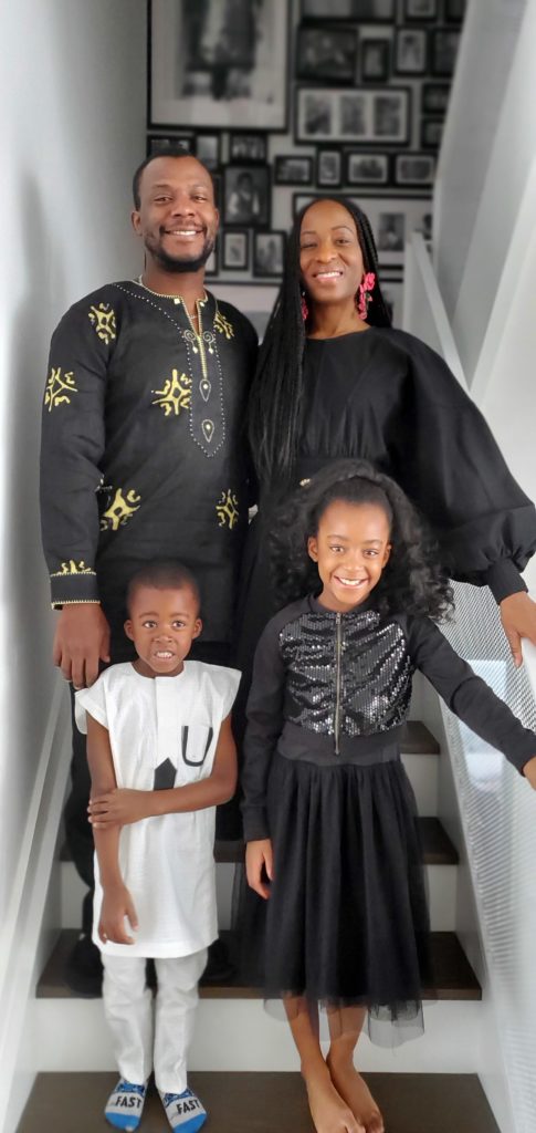 Racheal Awe stands on the staircase in her home with her husband and two young children.