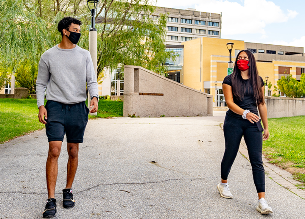 Two students wearing facemasks walk down the path in front of Vari Hall