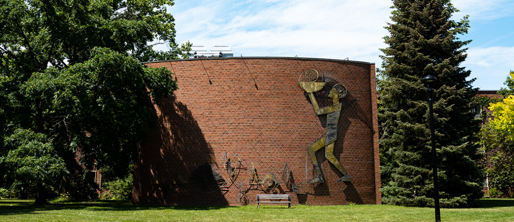 The Whole Person sculpture, metal pieces on a brick wall in the shape of a person holdnig a bowl above their head