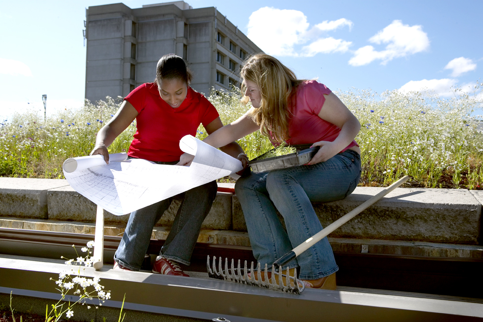 Two female students studying a technical drawing on the Faculty of Environmental and Urban Change rooftop, showing an example of Experiential Education (EE). 