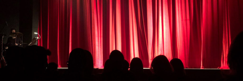 Red curtain on stage with audience in a darkened theatre