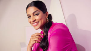 Lilly Singh in a pink blazer posing on her side with blue and back eyeliner