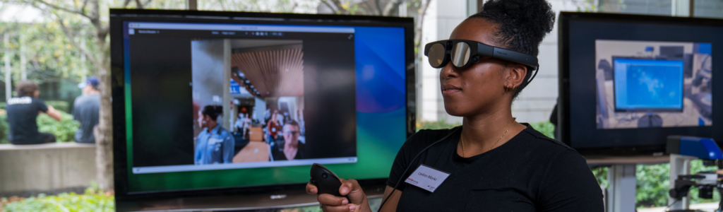 A Black woman wears an AI pair of glasses with a type of controller in one hand.