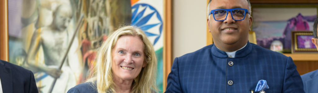 President Rhonda Lenton sands beside a South Asian man and they are both holding open portfolios with a signed letter on them