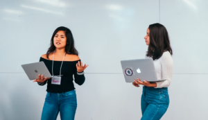 two students presenting their work, holding laptops