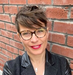 Jessica Parish with eyeglasses brick wall behind her