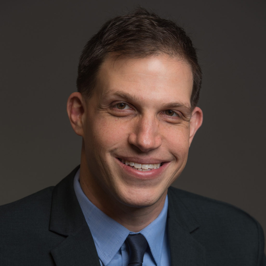 Sam Starr smiling wearing coat and blue tie