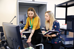 Two women are gathered around a table with a computer monitor on it.