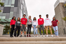 A group of eight students are standing on a flight of stairs in front of a glass building.