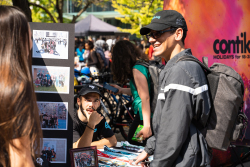 A boy is talking to a girl in front of an outdoor information stand.