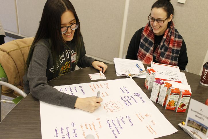 Two students working together on a table. One student is writing on a piece of paper.