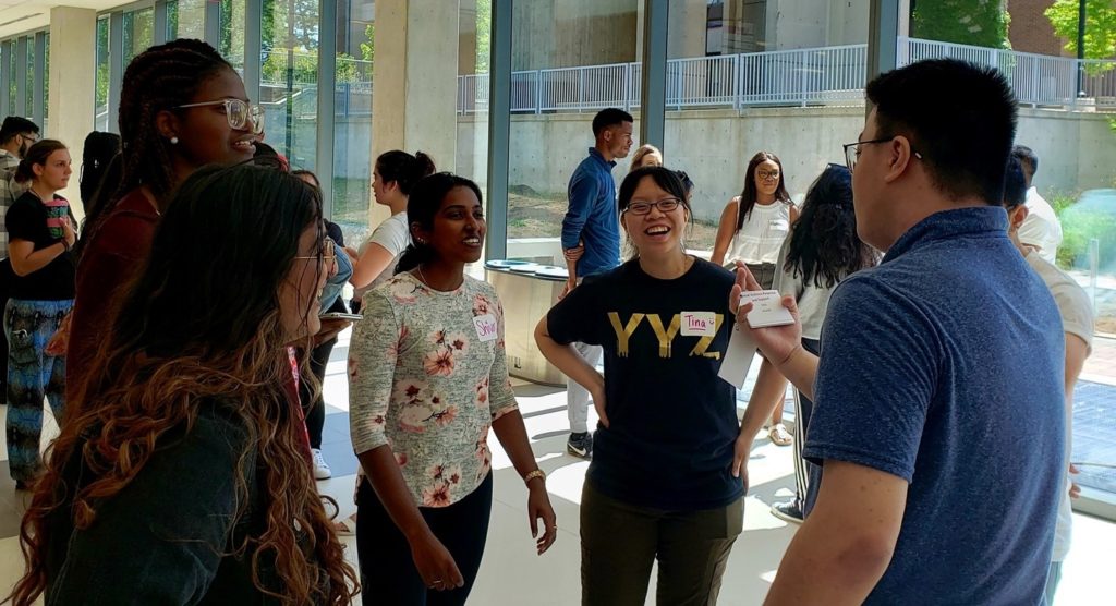 Five students standing in a circle laughing and talking together.