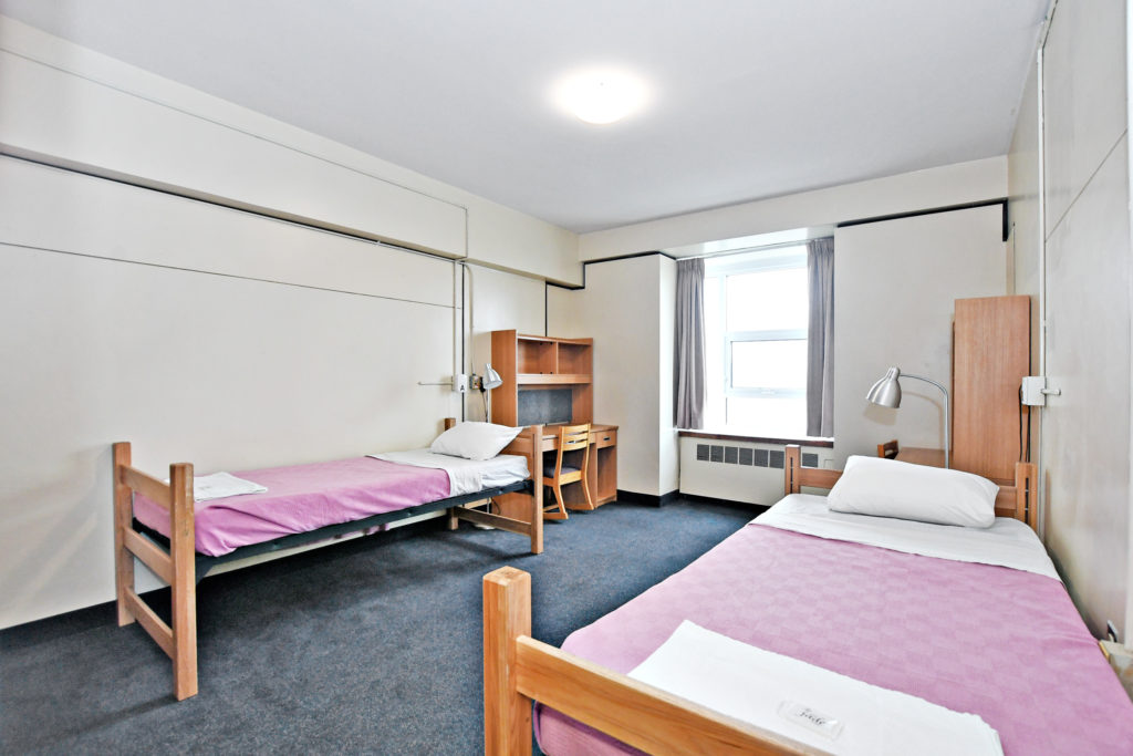 Interior of Vanier Residence. A double room with showing two beds and two desks with chairs.