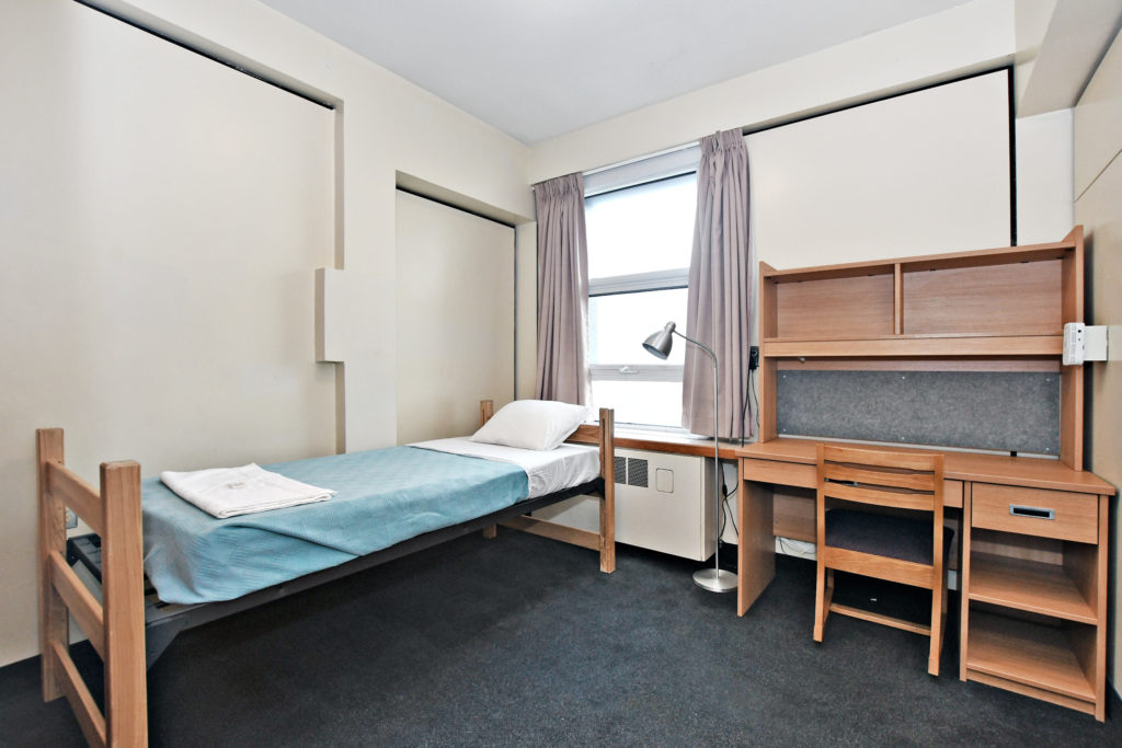 Interior of Vanier Residence. A single room showing bed and desk with chair.