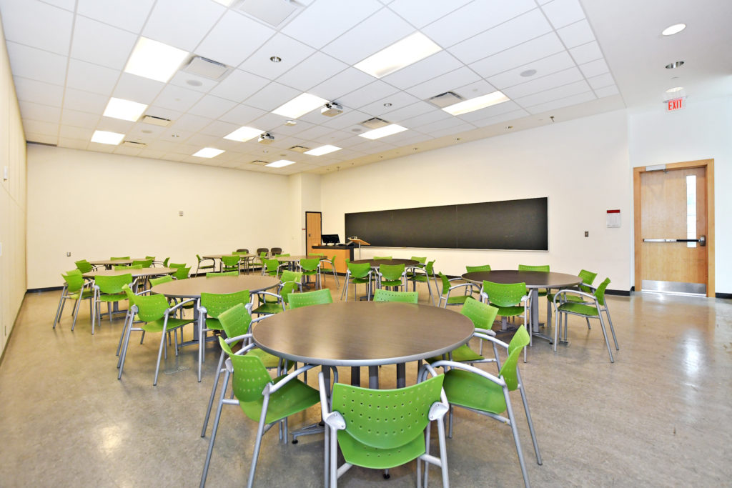 A classroom with several round tables surrounded by chairs.