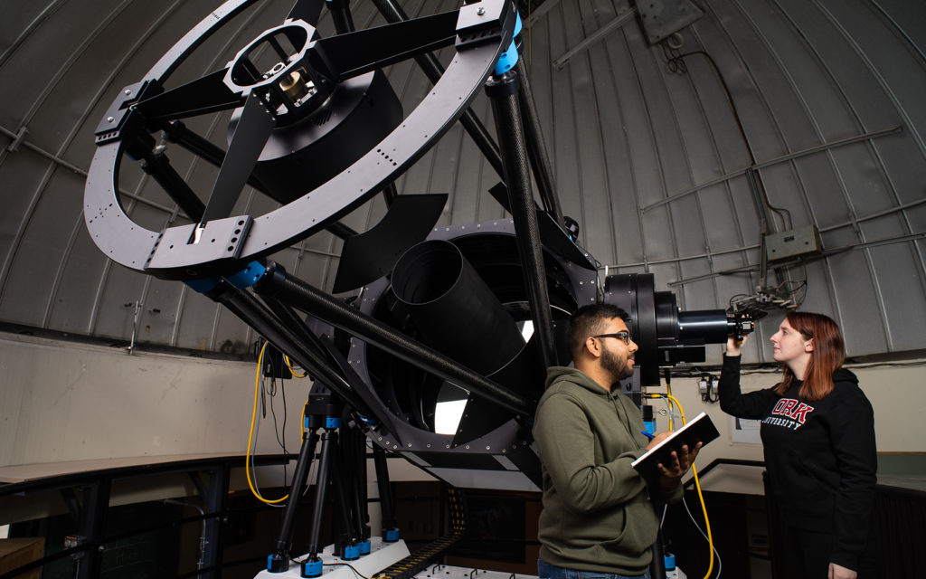 Two people standing beside a large telescope