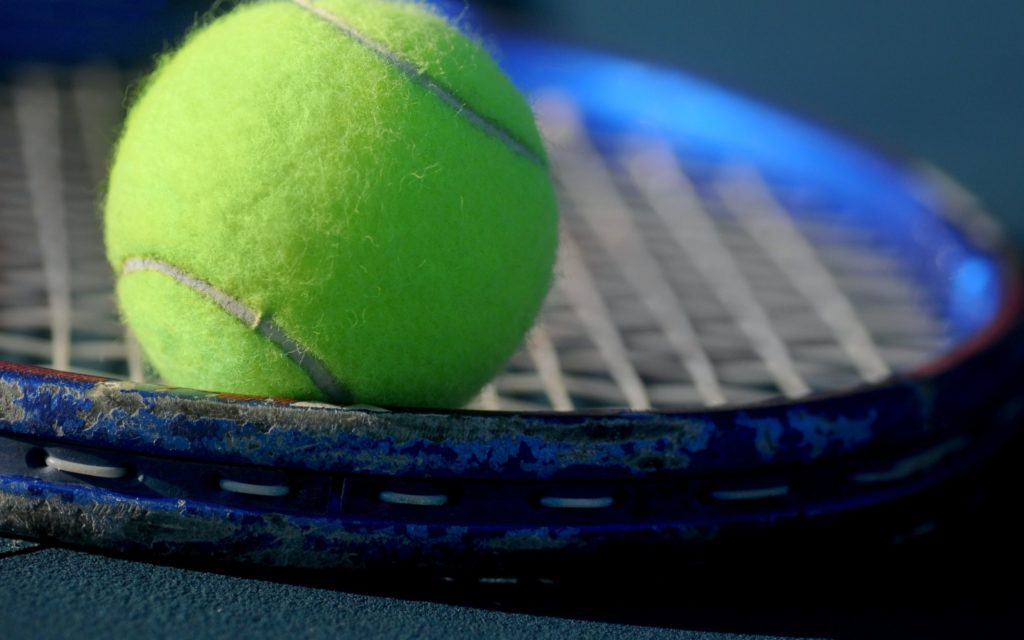 Green tennis ball resting on tennis racket in closeup