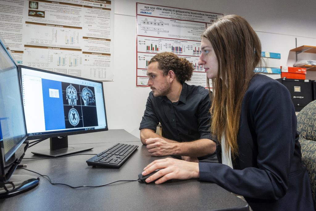Two people who are sitting look at a computer monitor displaying a brain CT scan.