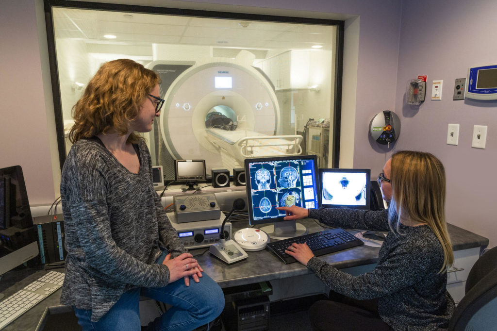 Persons points to an MRI scan on a computer monitor, to show the person beside them