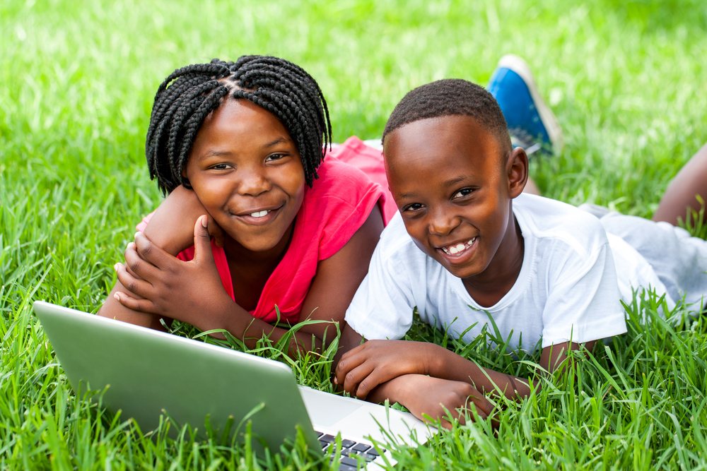 Two kids playing on a laptop in the grass