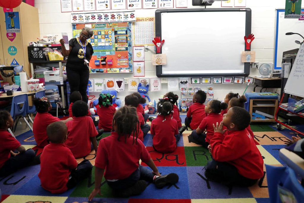 Classroom sitting on the floor with a teacher at the front.