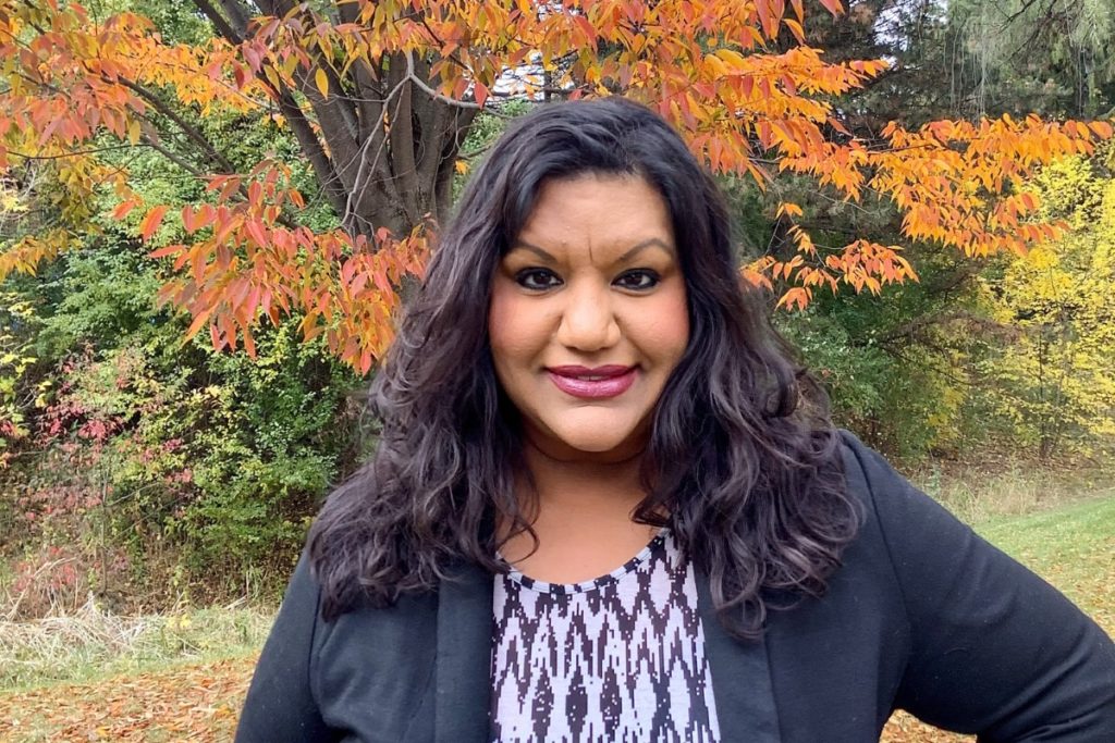 Vidya Shah standing in front of an autumn coloured tree