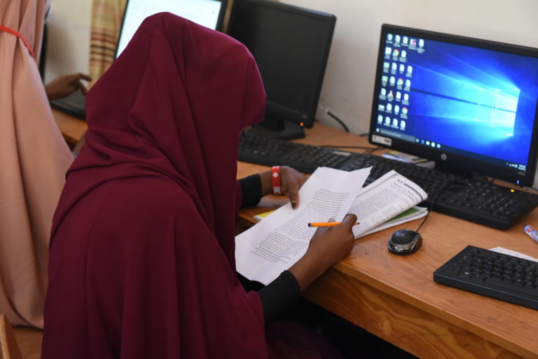image of a female student in a classroom sitting in front of a computer doing work at the Dadaab Education Centre.