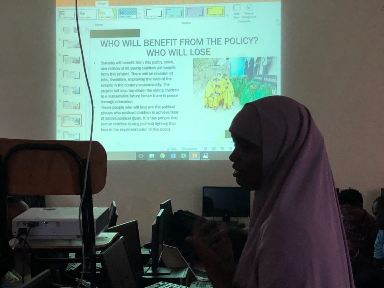 image of a female student in the Dadaab Education Centre in a classroom watching a Poerpoint presentation on a big screen.