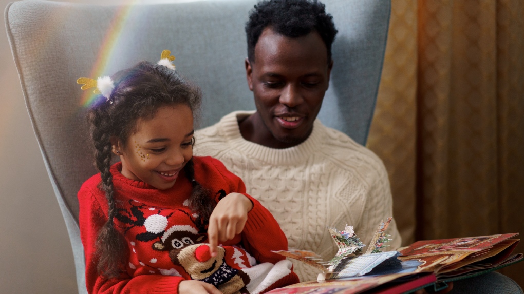 Parent and a child reading a pop-up book together. The child is wearing a reindeer sweater.