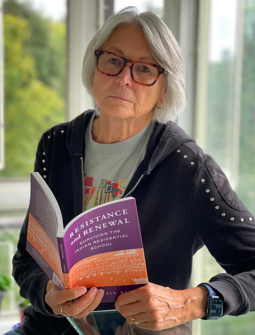 Celia Haig Brown sitting holding a copy of her book Resistance and Renewal: Surviving the Indian Residential School