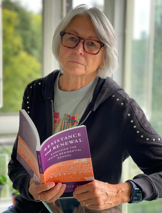 Celia Haig Brown sitting holding a copy of  her book Resistance and Renewal: Surviving the Indian Residential School