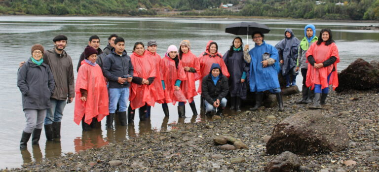 Pablo Aránguiz (second from left) pictured with students standing on the bank of a river in the rain. 