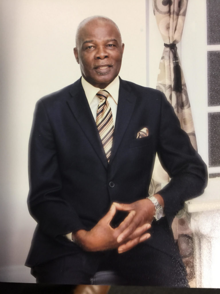 Glenford Duffus sitting and posing for a picture wearing a navy blue suit