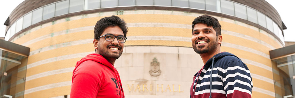 two males students of east asian descent standing in front of Vari Hall smiling