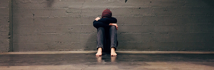 young homeless male sitting against a grey brick wall