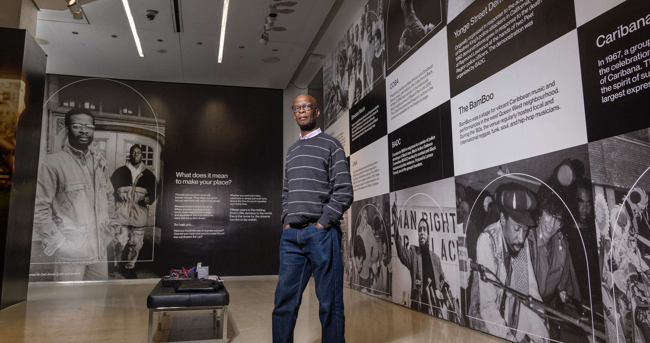 Professor Carl James standing in the lobby at the TIFF Lighbox with large mural images reflecting Black History in Toronto displayed on the walls of the lobby