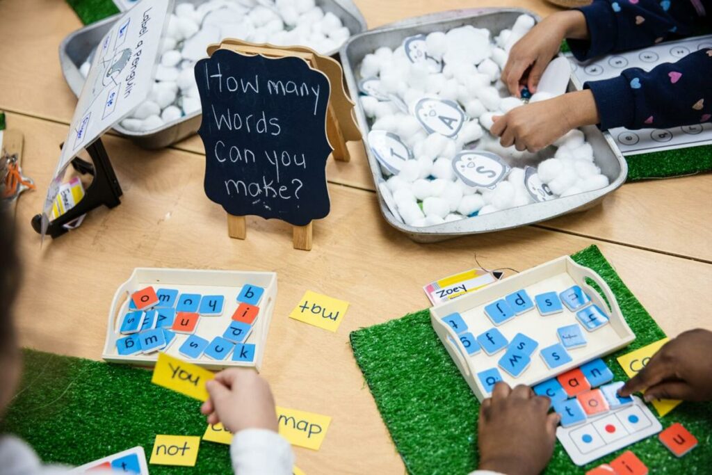 image of hands of a diverse group of kindergarten students working on a word creation exercise 