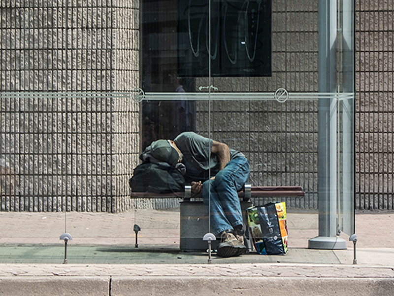 homeless man on a bench sleeping in a Toronto bus shelter