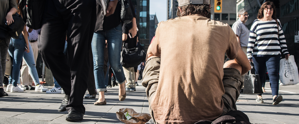 homeless man sitting on a busy street