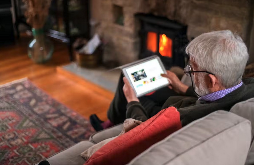 elderly man sitting in front of the fireplace scrolling on his laptop