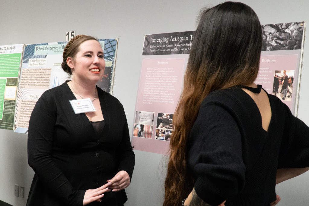 A poster presenter talking to a fellow student about their poster