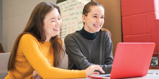 Two female students work on a laptop together.