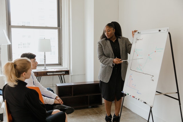 Woman in Gray Coat Standing Beside White Board while Discussing